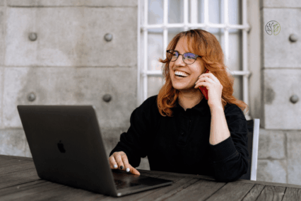 Sandra-Maria Kraus sitzt an einem Tisch mit offenem Laptop und telefoniert.