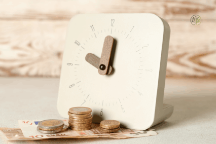 Eine Uhr mit Euro Münzen und Geldscheinen davor.