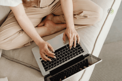 Frau sitzt am Sofa und arbeitet am Laptop